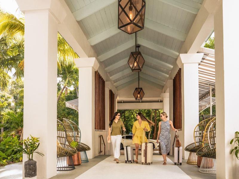 Überdachter Terrassengang mit weißen Säulen, Laternen und Pflanzen, drei Personen am Tisch.