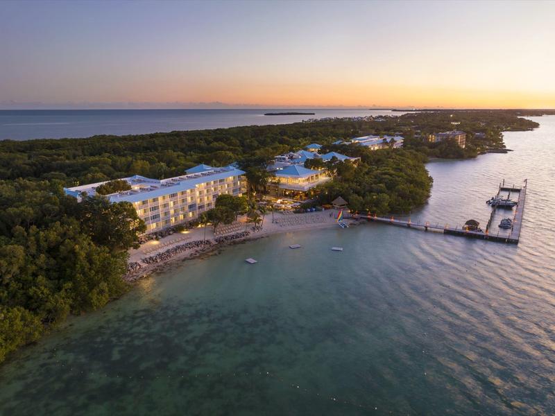 Luftaufnahme eines Resorts an einer Küste bei Sonnenuntergang mit Stränden und Bootsanlegern.