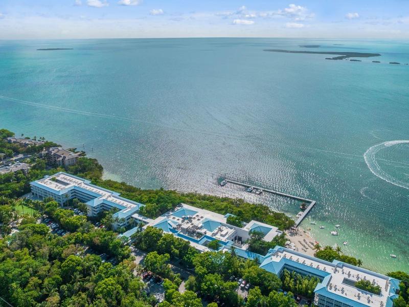 Küste mit Gebäuden, grünem Wald, blauem Meer und bewölktem Himmel im Hintergrund.