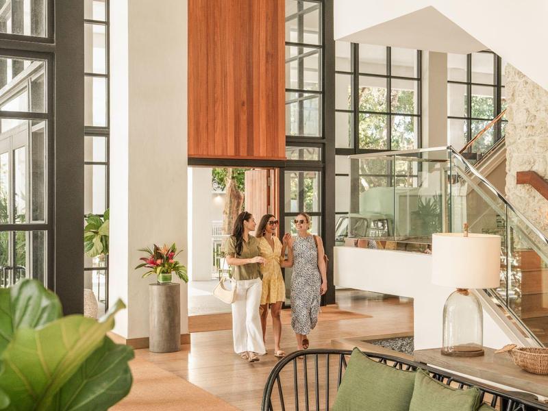 Helles Wohnzimmer mit zwei Frauen, großen Fenstern, Holzmöbeln und modernen Stilelementen.