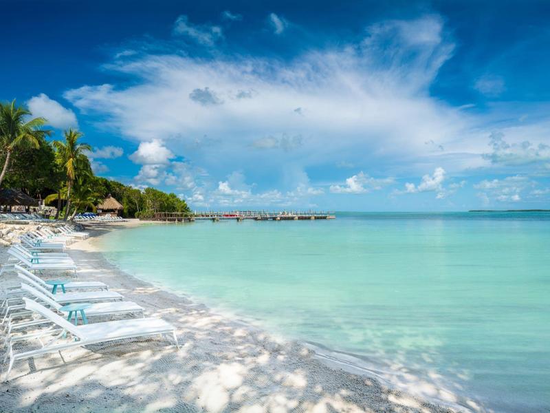 Weißer Sandstrand mit Liegestühlen, Palmen und türkisfarbenem Meer unter blauem Himmel