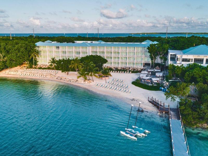 Strandresort mit Sandstrand, Bootssteg und grünem Wald am türkisblauen Meer.
