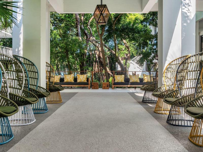 Moderner Außenbereich mit bunten Drahtstühlen, weißen Säulen und grünen Pflanzen im Hintergrund.