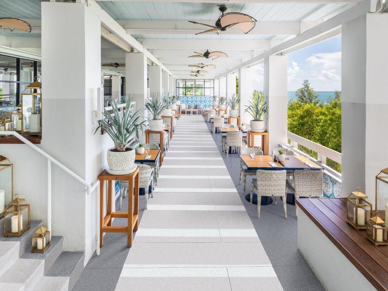 Moderner, heller Terrassenbereich mit Holz- und Metallmöbeln, weißen Säulen und dekorativen Laternen.