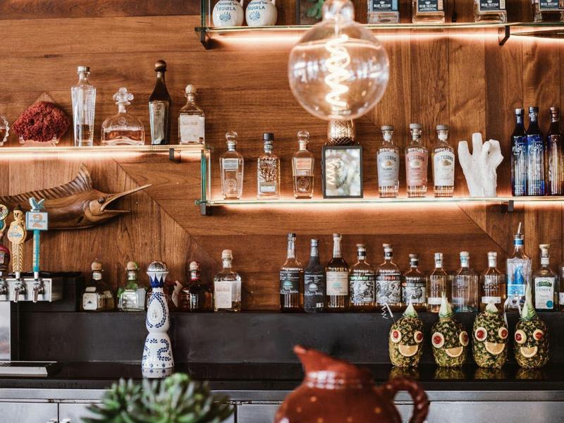 Bar mit Holzregalen voller verschiedener Spirituosenflaschen und Bierhähnen unter hellem Leuchtmittel.