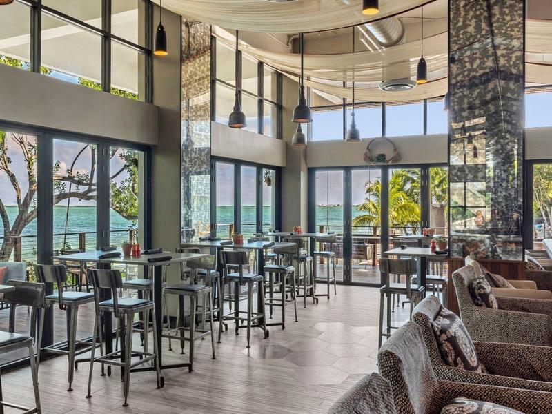 Modernes Café mit großen Fenstern, Holz- und Ledermöbeln, hoher Decke und viel Tageslicht.