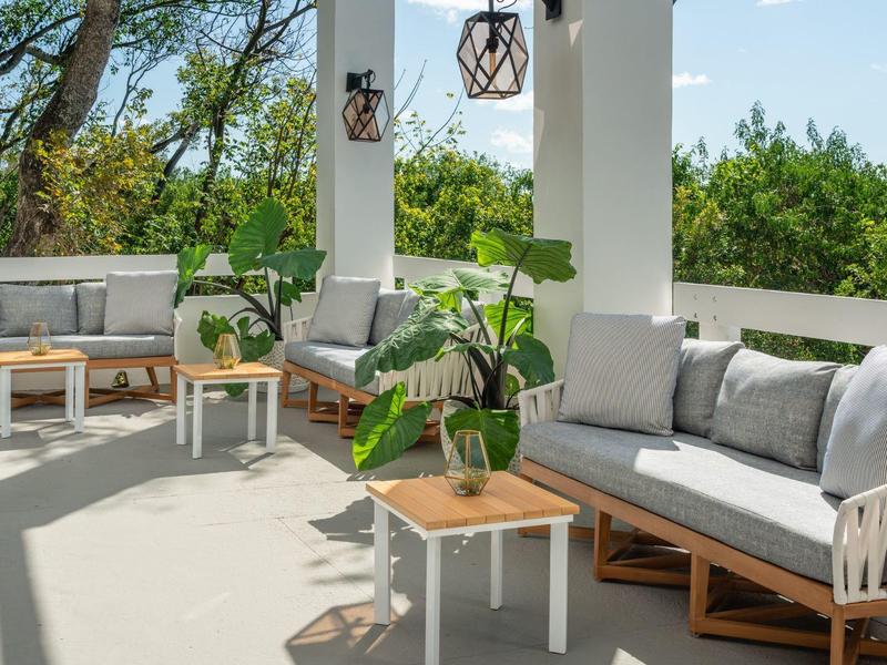 Gemütliche Terrasse mit weißen Säulen, Sitzgruppen aus Holz und Grau, Pflanzen und Blick ins Grüne.