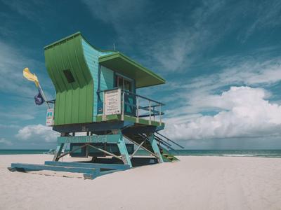 Grünes Rettungsschwimmerhäuschen auf einem ruhigen Sandstrand unter bewölktem Himmel.