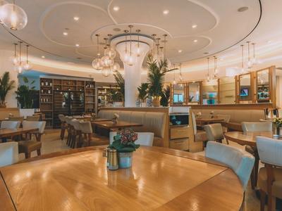 Eleganter Hotel-Dining-Bereich mit Holztischen, Sesseln und Blumendekoration unter einem kunstvoll gestalteten Deckenlicht.