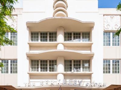 Modernes Hotel mit weißer Fassade, Terrasse und klar blauem Himmel im Hintergrund.