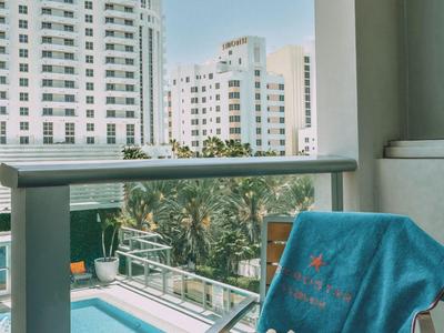 Blick auf einen Pool und hohe Hotels von einem Balkon mit Stuhl, Handtuch und Hut aus.