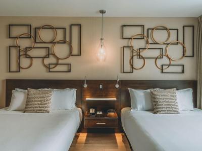 Modernes Hotelzimmer mit zwei Doppelbetten, stilvoller Wanddekoration und sanfter Beleuchtung.