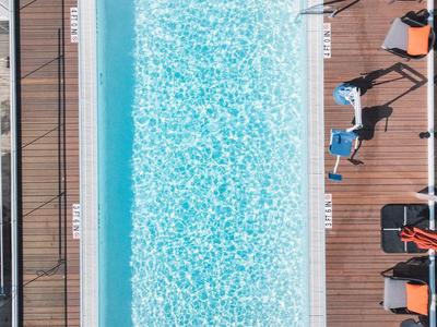 Vogelperspektive eines rechteckigen Pools mit blauen Wasser und umliegenden Sonnenliegen auf Holzdeck.