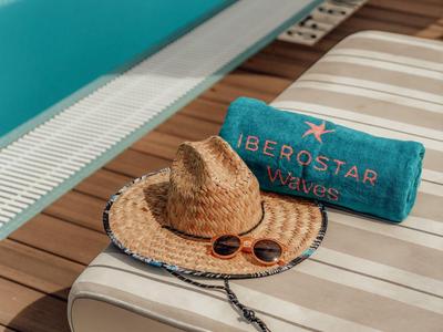 Strandliege neben Pool mit Strohhut, Sonnenbrille und türkisfarbenem Handtuch.