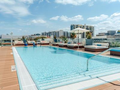 Moderner Hotelpool auf Dachterrasse mit Liegestühlen und Stadtblick bei Tageslicht.