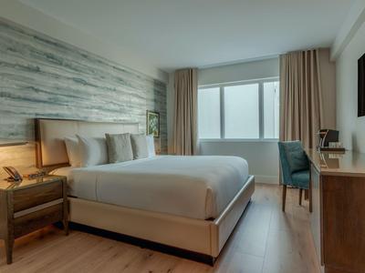 Gemütliches Hotelzimmer mit großem Bett, Holzfußboden, Stuhl und Schreibtisch neben Fenster.