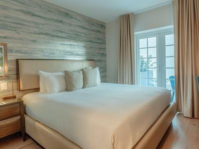 Hotelzimmer mit großem Bett, Holzverkleidung, Nachttisch und Zugang zum Balkon.