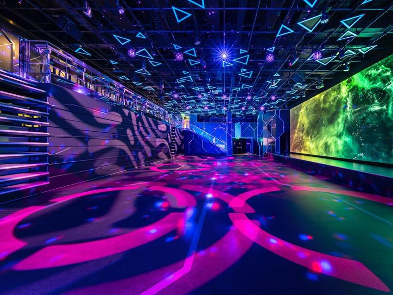 Moderner Nachtclub mit farbiger Beleuchtung und LED-Wand im Innenbereich.