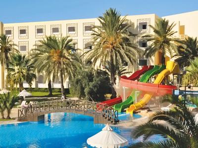 Hotelpool mit Palmen und bunten Wasserrutschen vor einem weißen Hotelgebäude