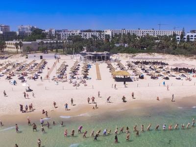 Breiter Sandstrand mit Liegestühlen und vielen Menschen am klaren Meer unter blauem Himmel.