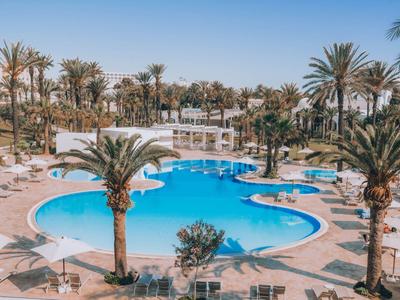 Großer, geschwungener Pool mit Palmen und Liegestühlen bei klarem Himmel.