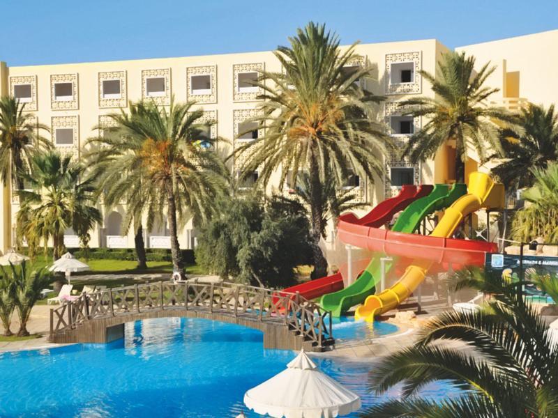 Hotelpool mit Palmen und bunten Wasserrutschen vor einem weißen Hotelgebäude