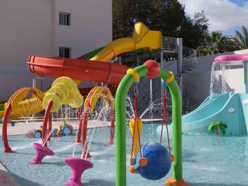 Kinderwasserrutsche mit verschiedenen bunten Wasserspielen in einem Hotelpoolbereich.