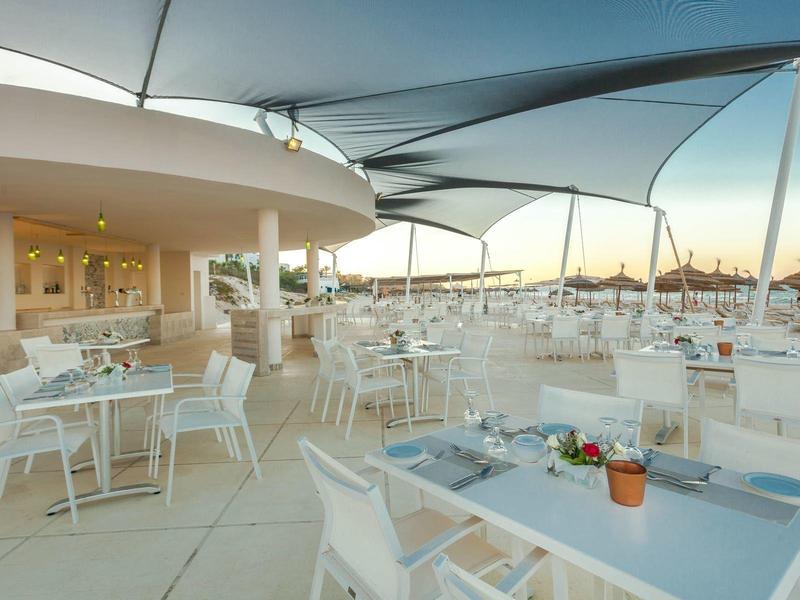 Dachterrasse mit weißen Tischen und Stühlen, Sonnenschutz und Blick auf Hotel und Hafen.