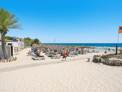 Strand mit hellem Sand, Liegestühlen, Palmen und blauem Himmel am Meer.
