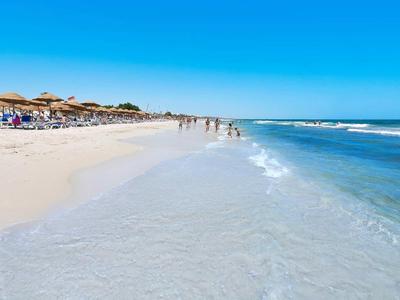 Breiter Sandstrand mit Sonnenschirmen, Menschen und klarem, blauem Meer unter blauem Himmel.