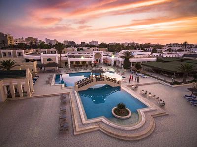 Hotelanlage mit Pools und Liegestühlen bei Sonnenuntergang unter einem bunten Himmel.