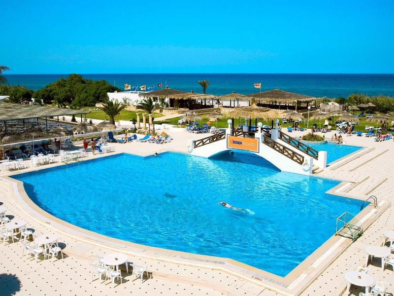 Großer Außenpool mit Sonnenschirmen und Liegen, Blick auf Meer und klare blaue Himmel.