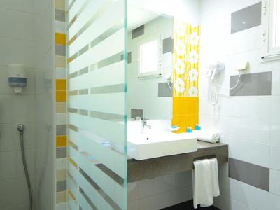 Helles modernes Badezimmer mit Dusche, großem Spiegel und gefaltetem Handtuch auf dunklem Boden.