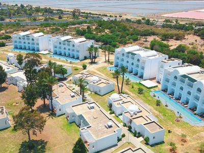 Luftaufnahme eines weißen Hotelkomplexes mit Pools, Palmen und Sandstrand im Hintergrund.