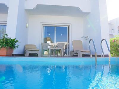 Ein klarer blauer Pool vor einer weißen Terrasse mit Tischen, Stühlen und grünen Pflanzen.