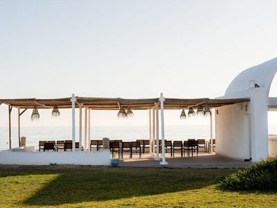 Open white pavilion with tables and chairs on a green lawn under clear sky.