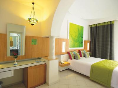 Modernes Schlafzimmer mit weißem Bett, bunten Kissen, grünem Wandbild und Schreibtisch mit Spiegel.