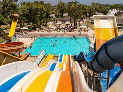 Mehrere bunte Wasserrutschen führen zu einem Schwimmbecken mit badenden Menschen im Freien.