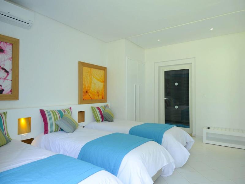 Bright hotel room with three single beds, colorful pillows, and modern wall art.