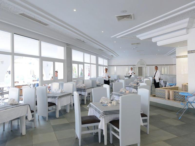 Bright, spacious hotel dining room with white chairs, tables, and large windows.