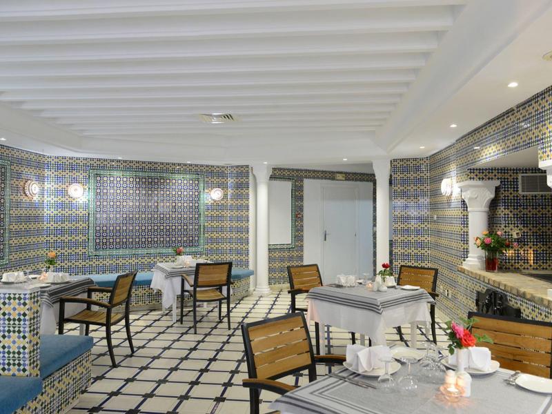 Indoor dining area with mosaic tile walls, white ceiling, and wooden chairs around tables.