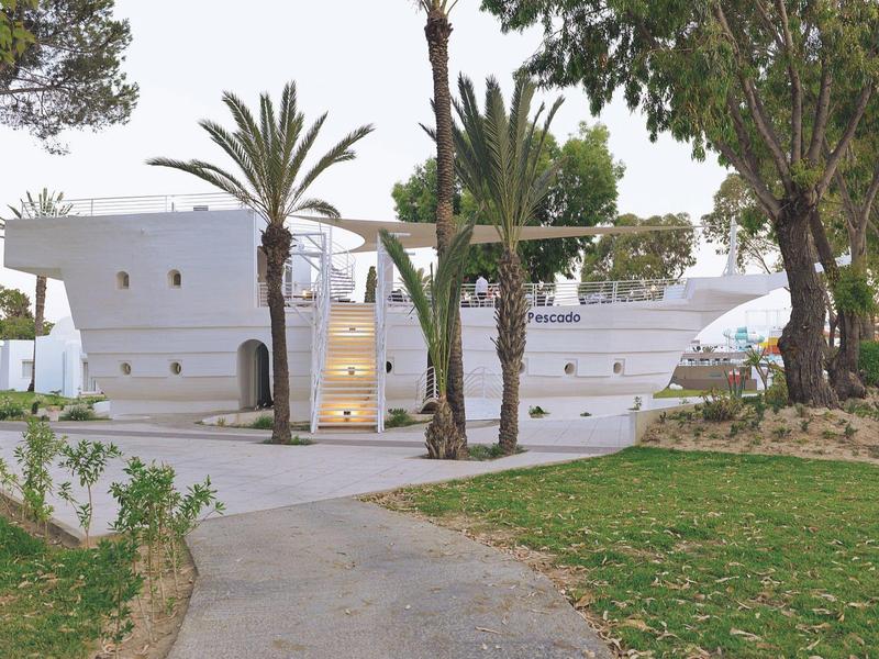 White boat-shaped hotel surrounded by trees and greenery.
