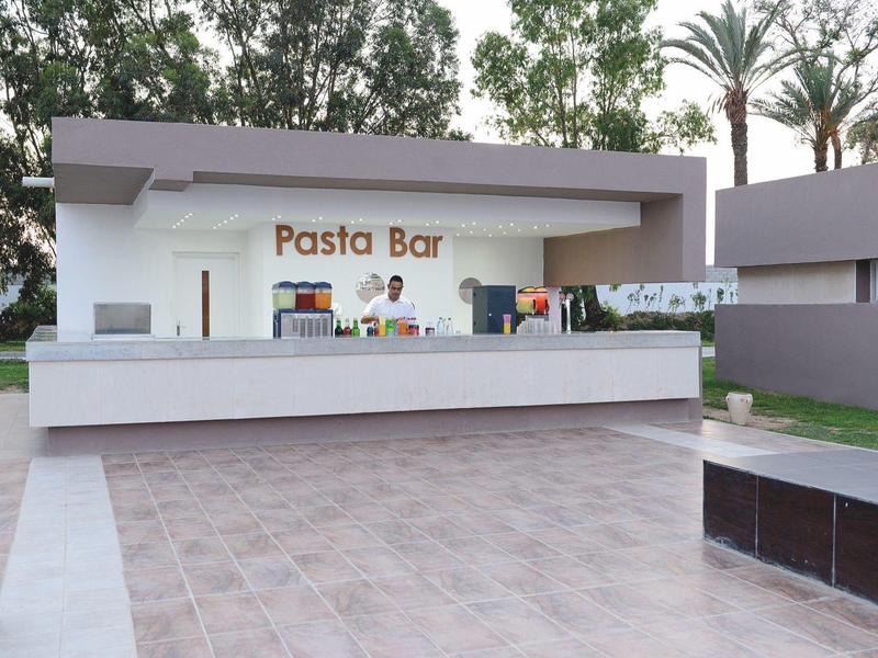 Outdoor pasta bar with white counter, seating, and palm trees in the background.