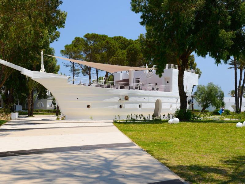 Modern white hotel building shaped like a ship, surrounded by trees and grass.