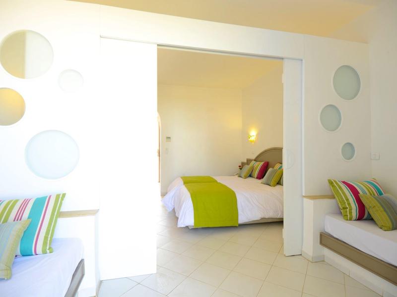 Bright hotel room with double bed, colorful cushions, and modern circular wall decor.