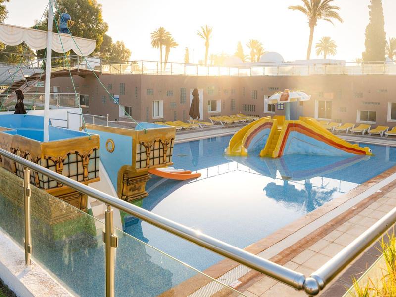 Children's pool with water slide and climbing frame at sunset in hotel