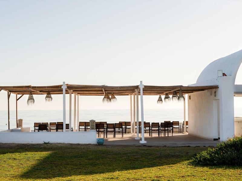 Open white pavilion with tables and chairs on a green lawn under clear sky.