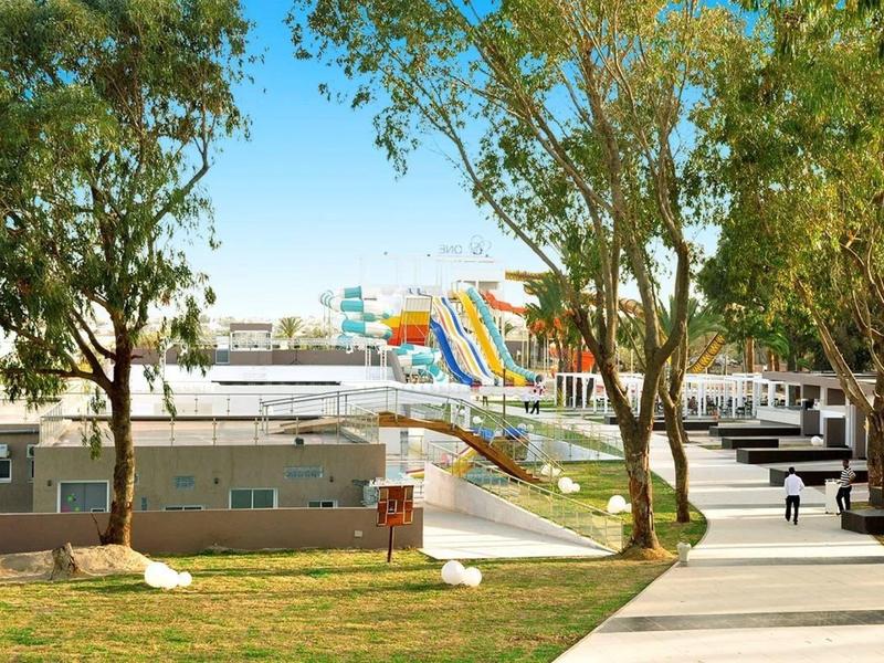 Water park with slides behind trees next to a walkway and grassy areas.