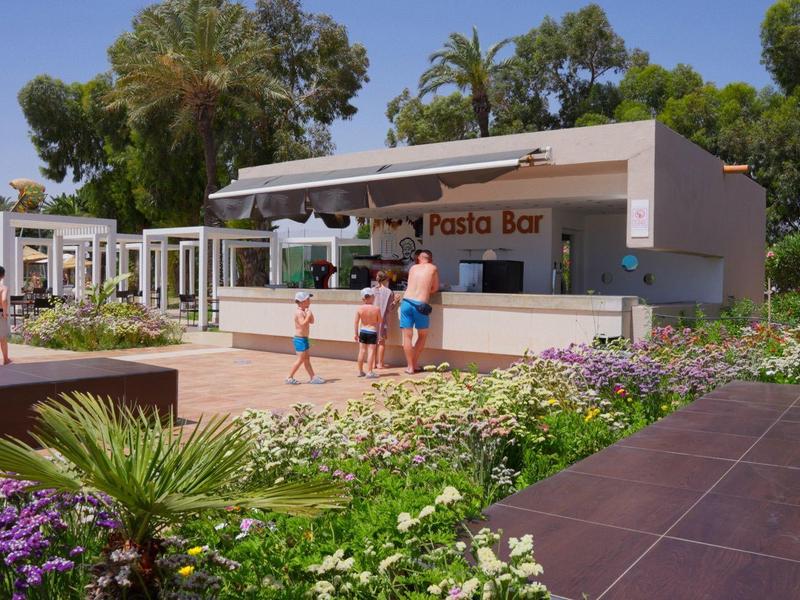 Pool bar surrounded by plants with umbrellas and guests on a sunny day.