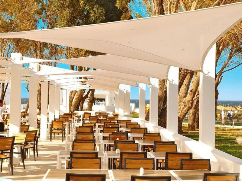Outdoor hotel area with rows of tables and chairs under white sunshade covers.